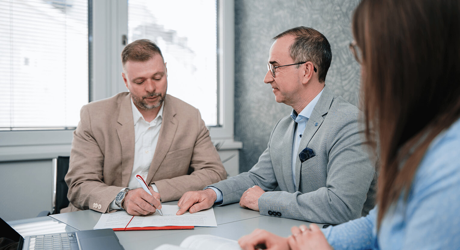 A képen egy szerződés aláírásának mozzanata látható, ahol Dr. Nemes Imre ügyvéd ügyfelét segíti az aláírás folyamata során. Az iroda modern és professzionális környezetet biztosít a munkavégzéshez, valamint bizalmat és határozottságot sugall az ügyfelek számára.